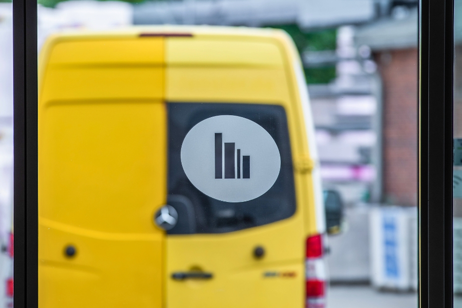Gelber Lieferwagen steht vor einer Glastür, auf dem das Logo von CAPITAL Baustoffe zu sehen ist.