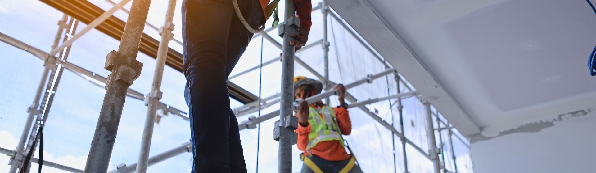 Zwei Menschen sind auf einem Baustellengerüst gesichert, stehen auf dem Gerüst, es ist von der Gebäudeinnenseite aus fotografiert
