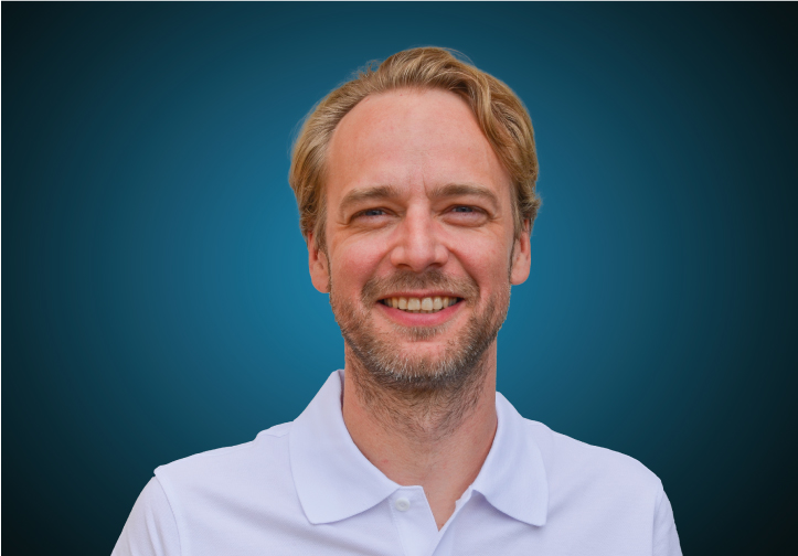 Portraitfoto eines Fachberaters für Bauelemente im Innendienst von CAPITAL Baustoffe vor einem blauem Hintergrund