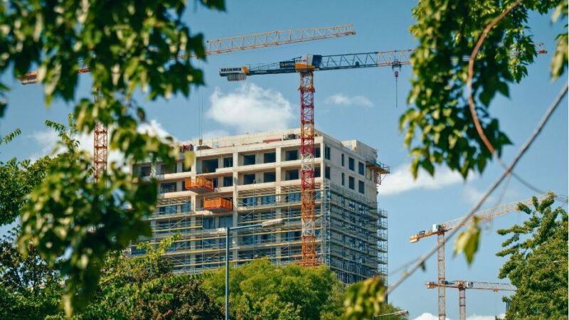 Hochhaus im Bau, gelber Kran umrandet von Blättern.